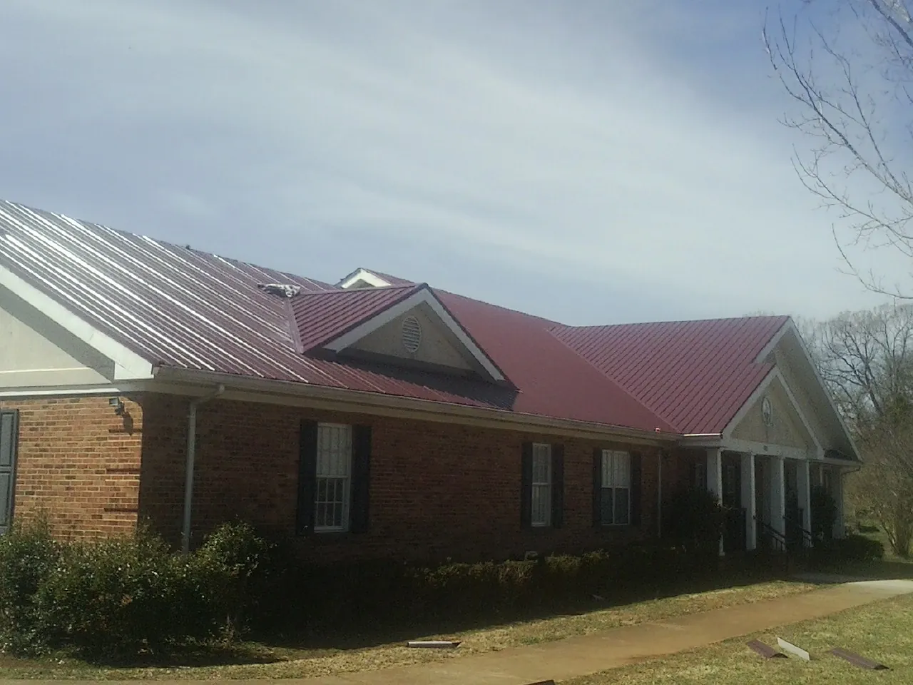 Red metal roof with gabled entries on a long brick building, from a Hail Damage Roof Repair job in Altona