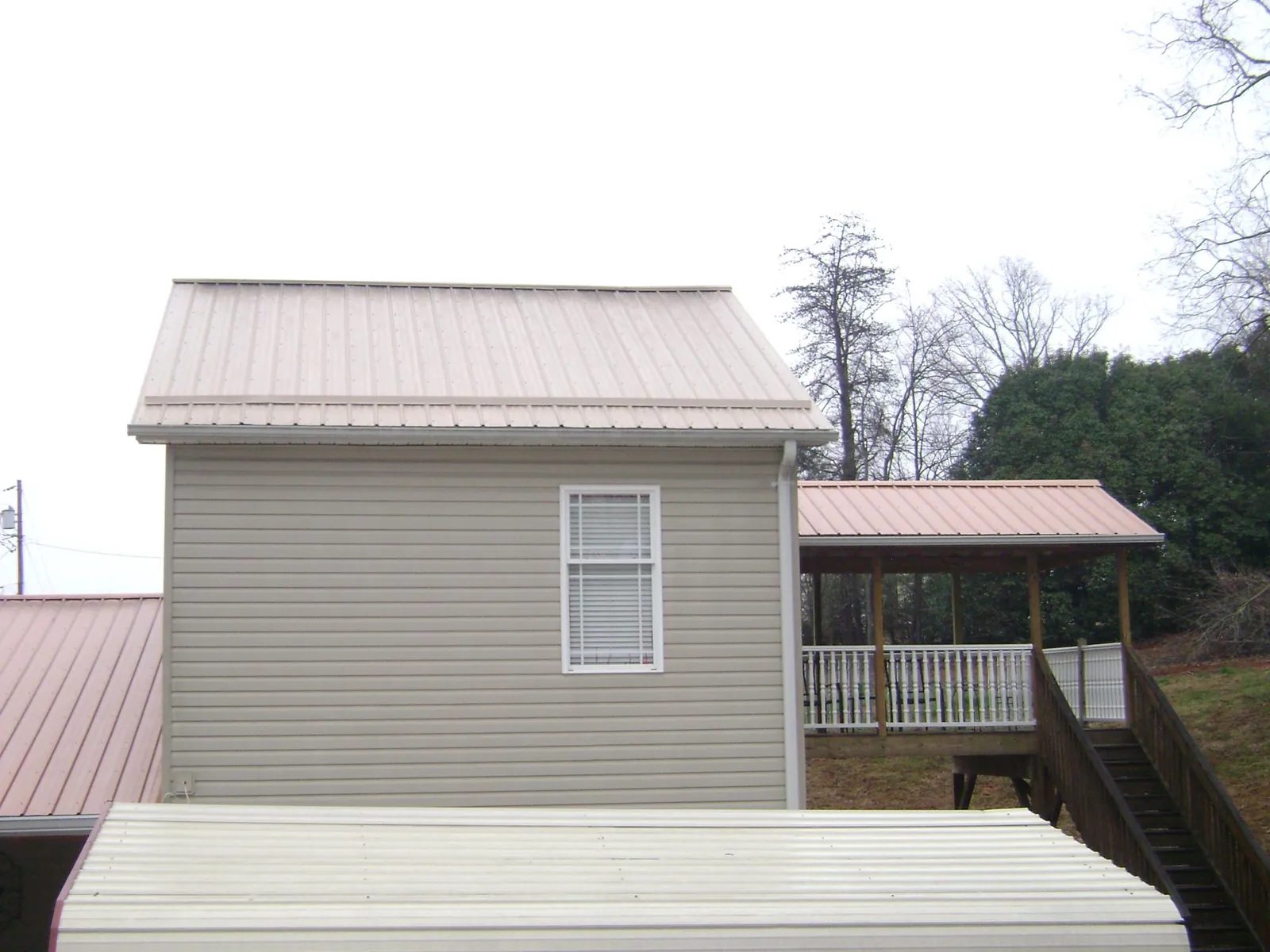 Tan metal roofs on a two story addition and attached porch, from a Roof Replacement job in Altona